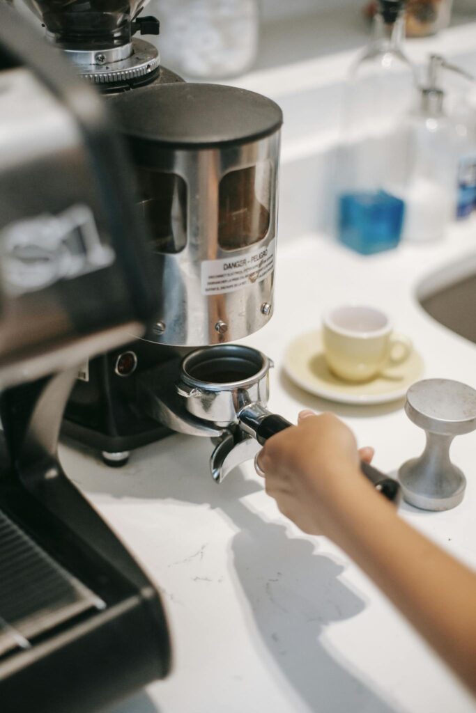 From above of crop unrecognizable barista with portafilter near coffee maker preparing hot drink in cafe